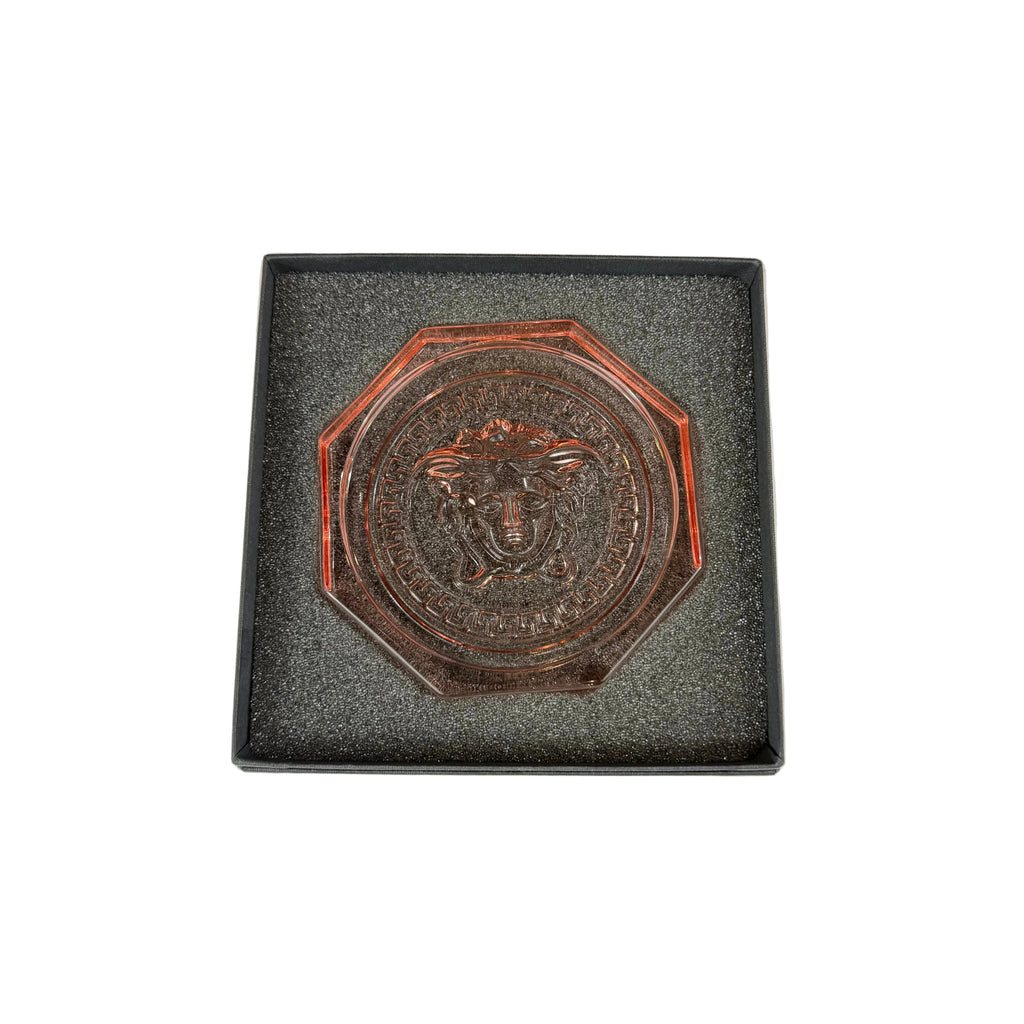 Bronze medallion with a face design on a gray cushioned base against a white background