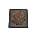 Bronze medallion with a face design on a gray cushioned base against a white background