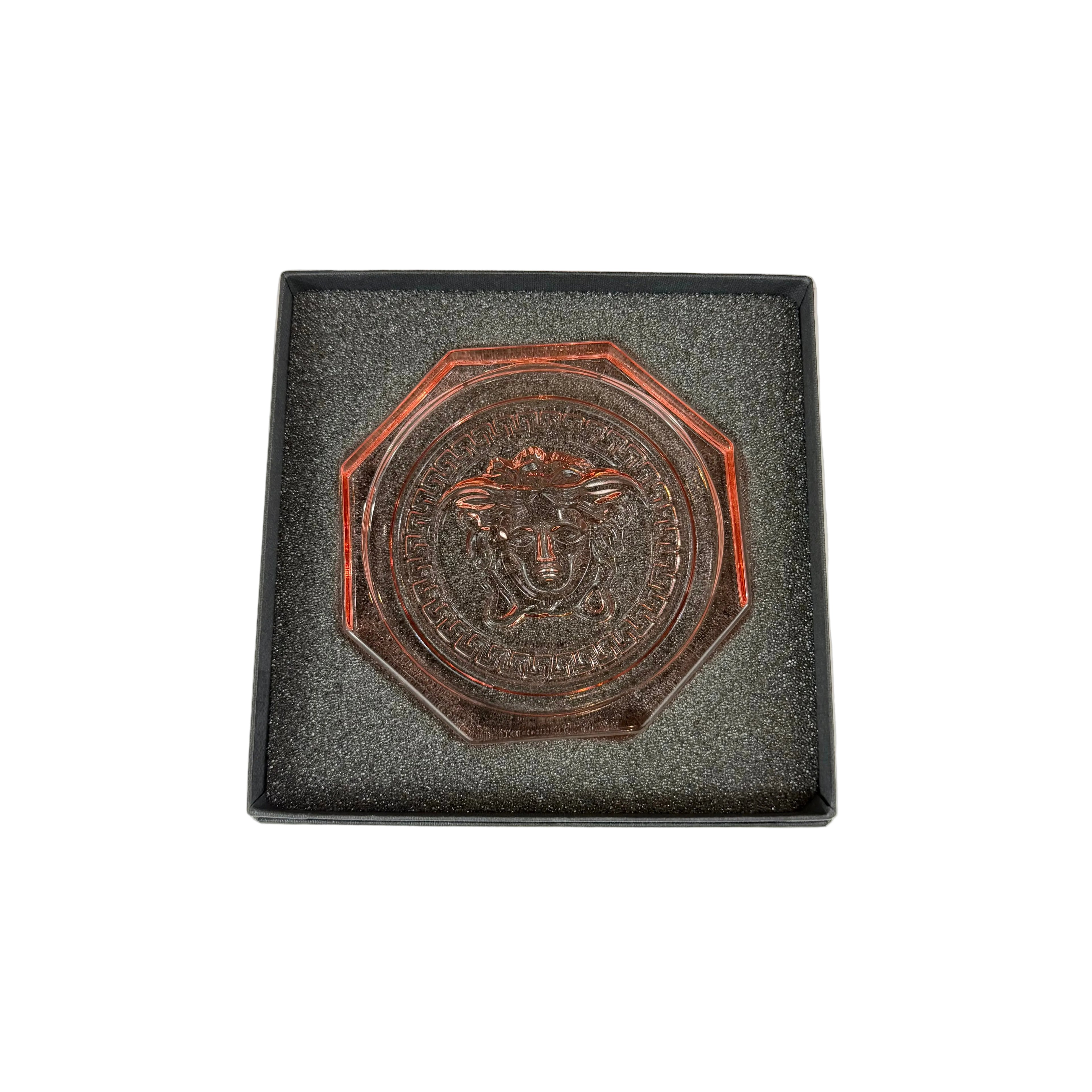 Bronze medallion with a face design on a gray cushioned base against a white background