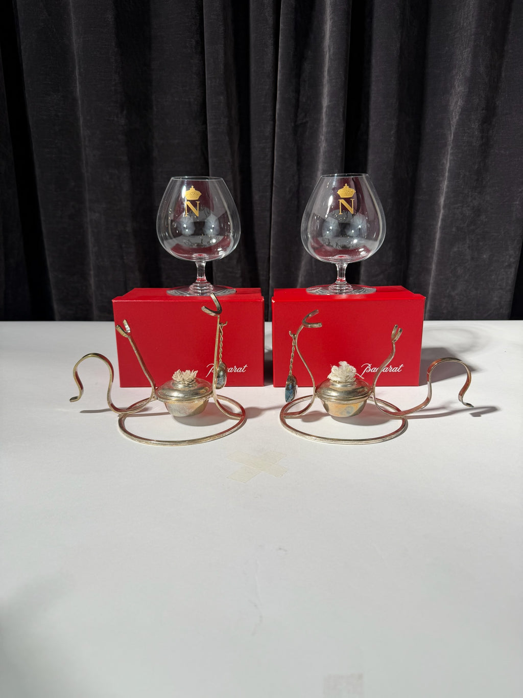 Two glass snifters with decorative elements on a white surface against a dark curtain background.
