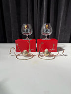 Two glass snifters with decorative elements on a white surface against a dark curtain background.