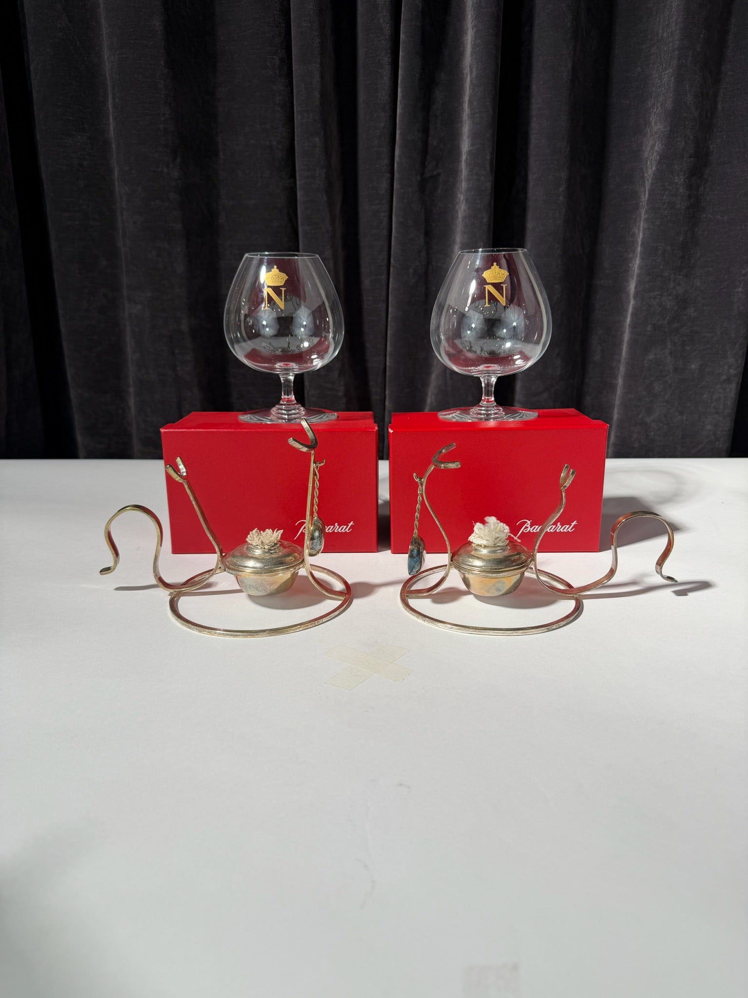 Two glass snifters with decorative elements on a white surface against a dark curtain background.